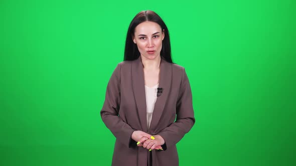 Female Reporter in Suit Looks Into the Camera and Speaks Into a Lavalier Microphone on a Green
