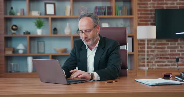 Bearded Ceo in Business Suit which Posing on Camera During His Work on Laptop in Modern Office