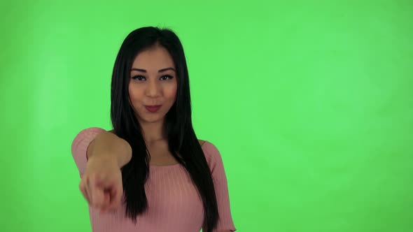 Young Attractive Asian Woman Points To Camera - Green Screen Studio