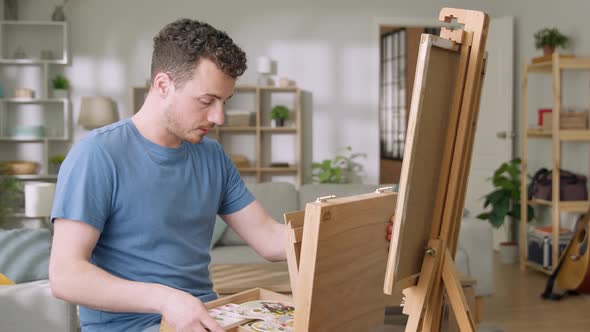 Young Man is Working in His Modern Home Studio in the Morning Drawing on Canvas Enjoying the Process