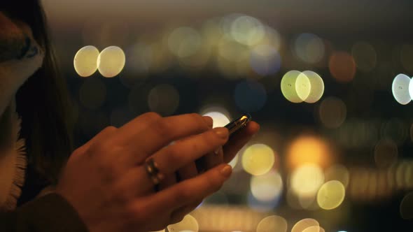 Super Close-up on Female Hands Using Smartphone Shopping App at Amazing Bokeh Sunset City Lights