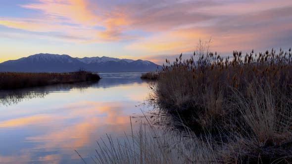 Colorful sky reflecting off a large lake just before the sun peaks from behind the distand mountains