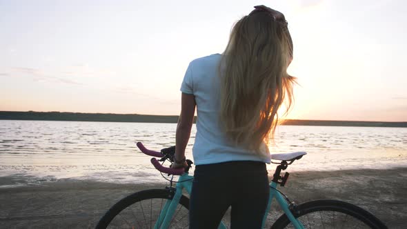 Young Attractive Woman Riding Biycle on the Beach Near the Sea During Sunrise or Sunset Slow Motion