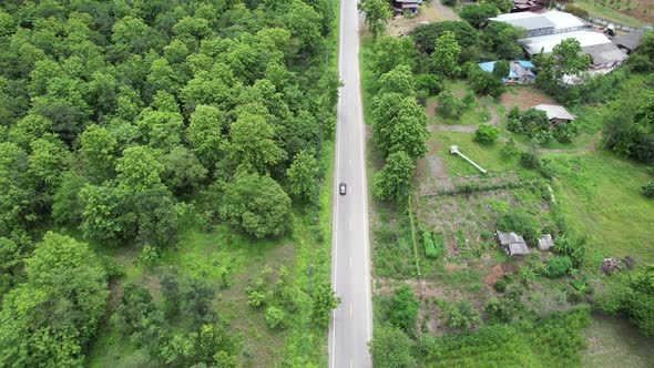 Aerial view of a car running along the mountain road through tropical forest in countryside by drone