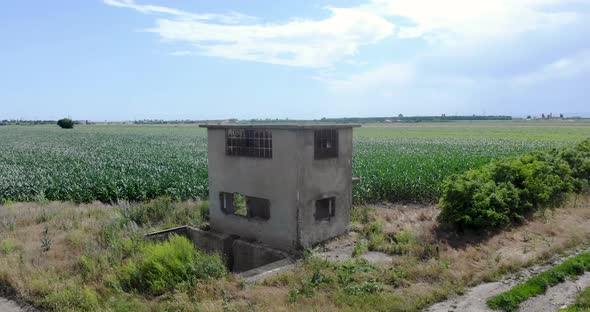 Old And Abandoned Concrete Building At Corn Fields In Countryside On A Sunny Day. - aerial