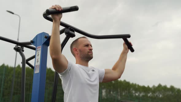 Male Bodybuilder Performing Exercises with a Heavy Weight for the Back on a Simulator on an Outdoor