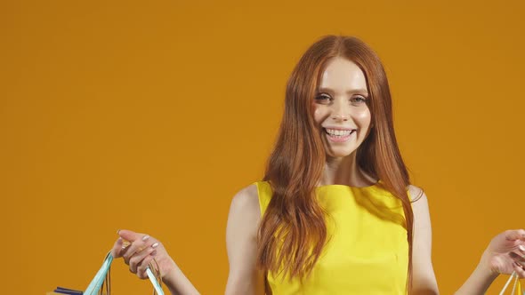 Cheerful Lady in a Yellow Dress Poses with Colorful Shopping Bags on an Isolated Yellow Background