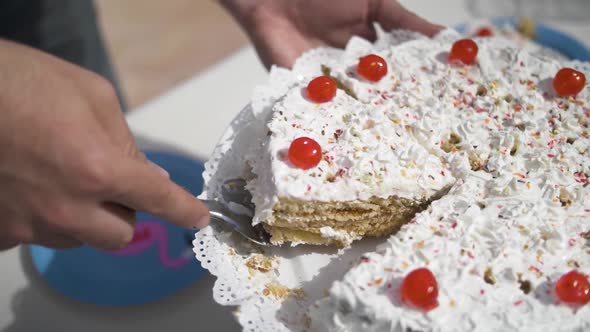 Woman´s hand serving a piece of white cream cake with red candy cherries on a sunny summer event at