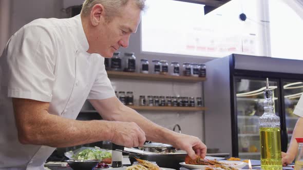 Caucasian male chef wearing chefs whites in a restaurant kitchen, putting food on a plate