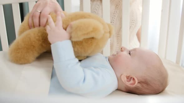 Happy Smiling Baby Boy Palying and Holding Teddy Bear While Lying in Wooden Cradle