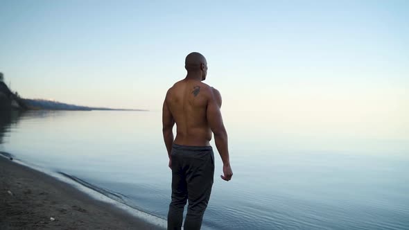 Athletic man looking out across the water on a beach in slow motion