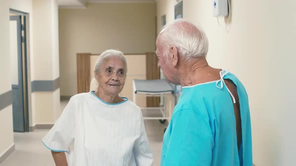 Old gray-haired woman standing in hospital corridor with old man