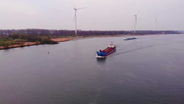 Aerial View Over Oude Maas On Overcast Day With Still Wind Turbines On Rivers Edge And Cargo Ships A