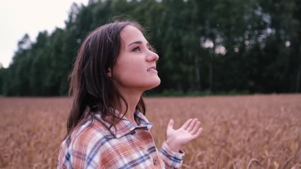 Happy Young Tourist Woman in a Plaid Shirt Looks Up with Raised Arms, Enjoying a Calm Rainy Day in