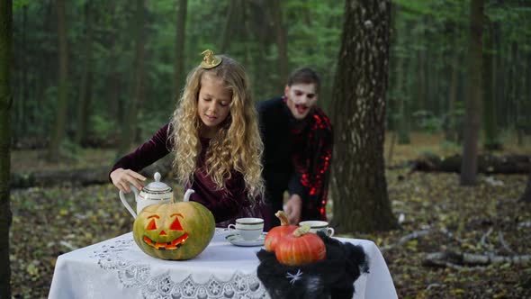 Little Girl Pouring Tea in Cup As Scary Vampire Coming From Forest at Background
