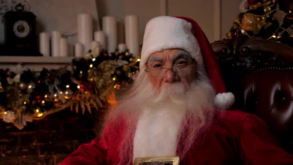 Close Up Santa Claus Looks Camera Sitting on Chair at Home Christmas Holidays