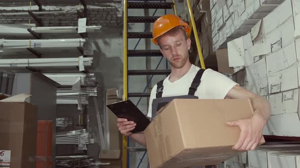 Factory Man Is Checking Cardboard Box and Looking at the Clipboard in Warehouse