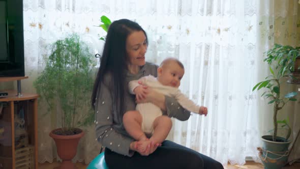 A Young Mother in the Living Room Doing Gymnastics with the Baby Rehabilitation on a Gymnastic Ball