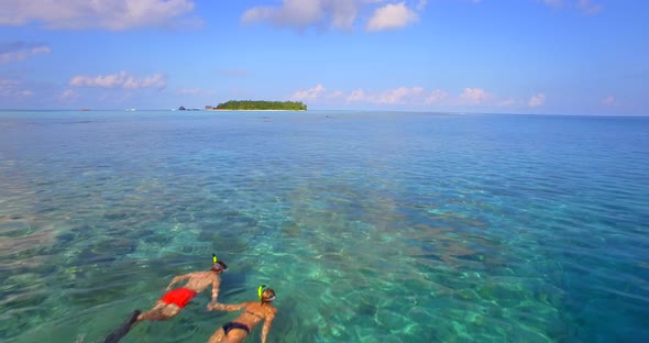 Aerial drone view of a man and woman couple snorkeling over the coral reef of a tropical island.