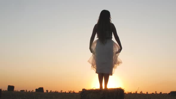 silhouette girl figure enjoying sunset in field,young woman walking on nature on haystack