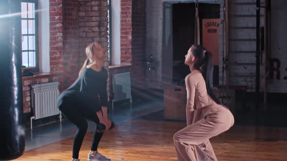 Two Women Training Together in the Gym  Squatting with a Dumbbell in Front of Each Other