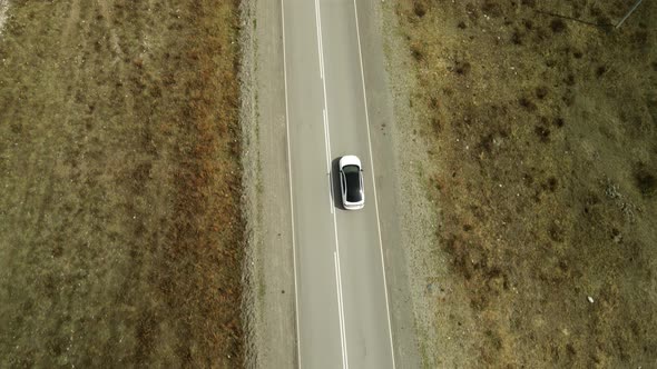 A White Car is Moving Along the Road Along the Steppe