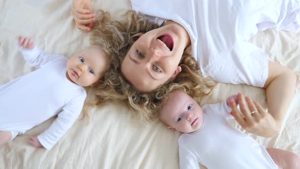 Happy Mother Lying On Bed With Her Two Baby Girls.