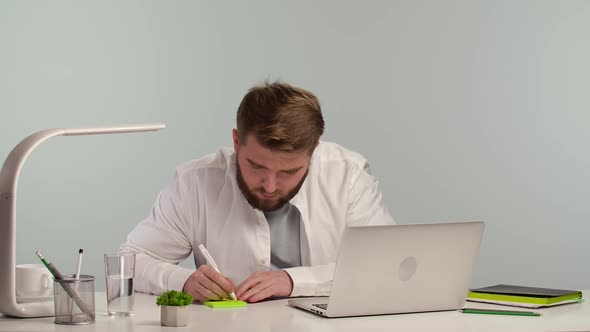 Serious Young Man Sitting at Desk in Home Office Taking Notes Working Remotely