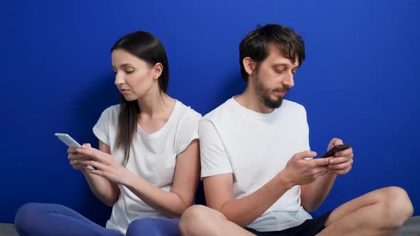 Man and Woman Are Sitting with Phones on the Bed at Home on the Background