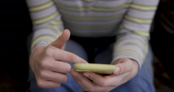 Close up shot of woman hands using a smart phone while sitting on the sofa at