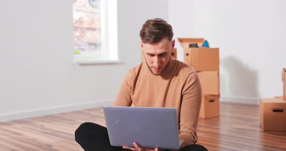 Smiling Caucasian Handsome Young Teenage Boy Sitting on the Floor in New Apartment and Thinking