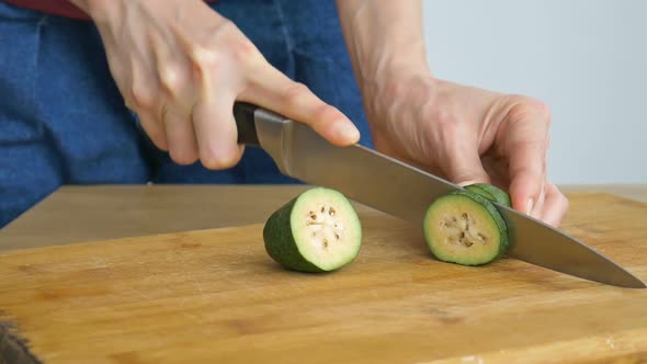 Female Hands is Cutting a Fresh Green Feijoa Fruit on a Cut Wooden Board