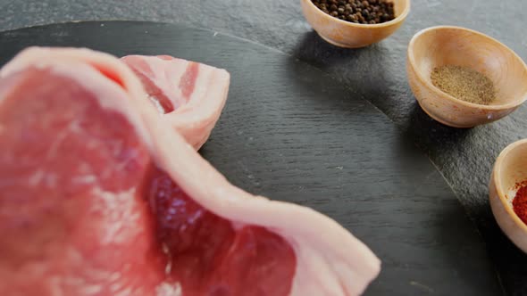 Sirloin chop and bowls of spices on concrete background