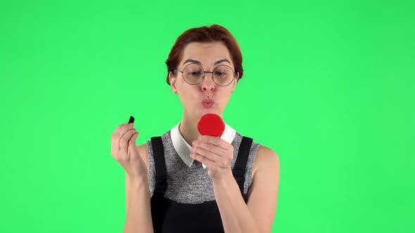 Portrait of Funny Girl in Round Glasses Is Painting Her Lips Looking in Red Mirror. Green Screen