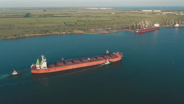 Aerial View of a Large Cargo Ship Leaving the Harbor with Tugboats at Sunset