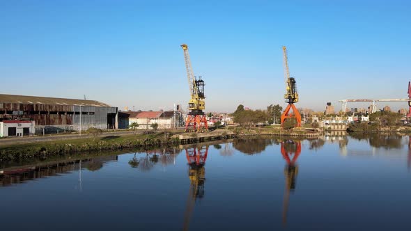 4K Aerial Drone Footage of Two Large Cranes Along the Water Edge with Clear Reflections Next to a Wa