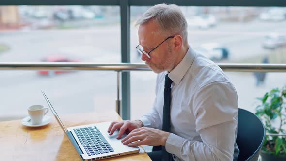 Serious businessman typing on a computer indoors on city background