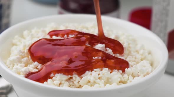 Berry syrup pouring into bowl of cottage cheese