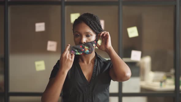 Young African Businesswoman Stands in Conference Room, Woman Puts on a Cloth Mask To Protect Himself