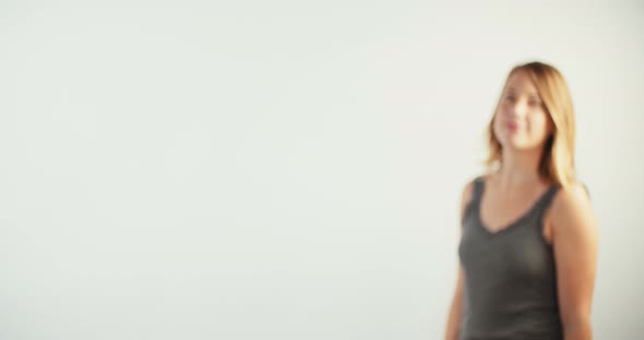 Young blond woman walking up to the camera and smiling on white studio background