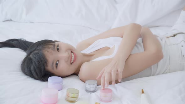 Beautiful of young asian woman smiling and lying on bed at bedroom, beauty of girl touch cheek.