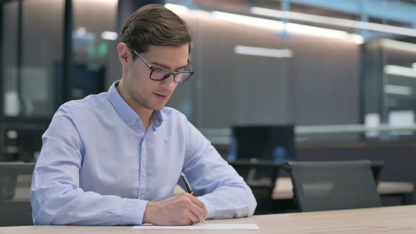 Pensive Young Man Writing on Paper Thinking