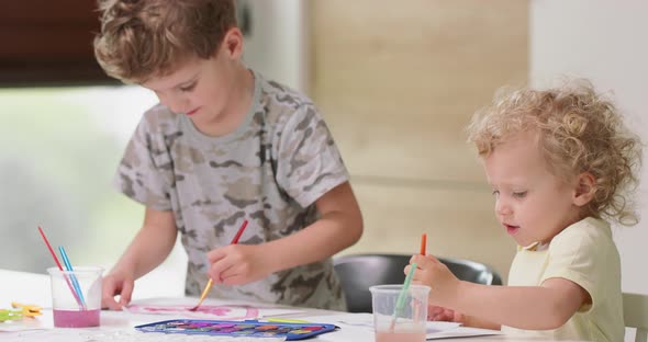 Brother and Sister Draw Watercolors While Sitting at the Table Girl Tries to Soak Paintbrush in