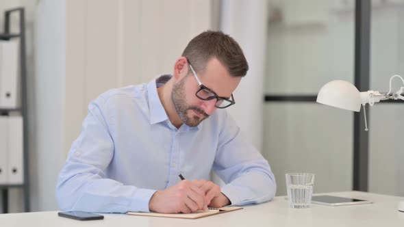 Middle Aged Man Writing on Paper at Work