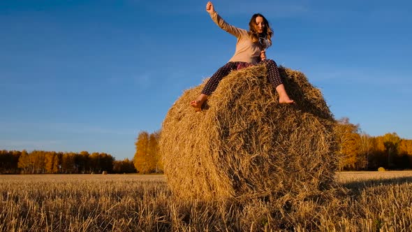 Beautiful Laughing Young Woman Sitting on a Haystack and Dancing