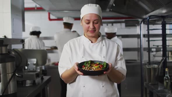 Portrait of caucasian female chef presenting dish and looking at camera