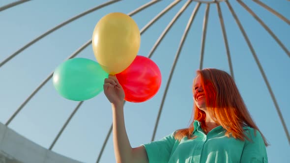 Beauty girl with red hair and colorful air balloons spinning and laughing, on white background. Beau