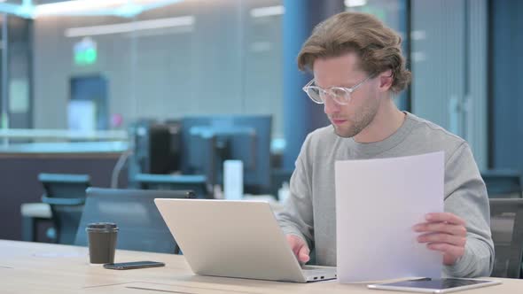 Businessman with Laptop Reading Documents in Office