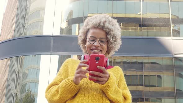 Smiling Afro American Woman on the Street Chatting with Smartphone