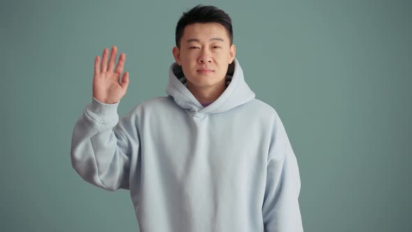 Handsome Asian man wearing hoodie waving at the camera